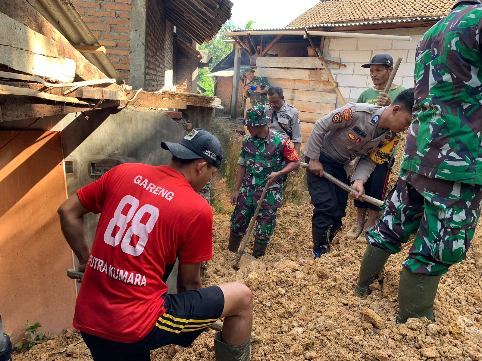 Sejumlah personel TNI-Polri bersama warga kompak bergotong royong membersihkan material tanah longsor yang menimpa salah satu rumah warga tepatnya di desa Depok Kecamatan Bendungan, Kabupaten Trenggalek. Rabu, (6/3).